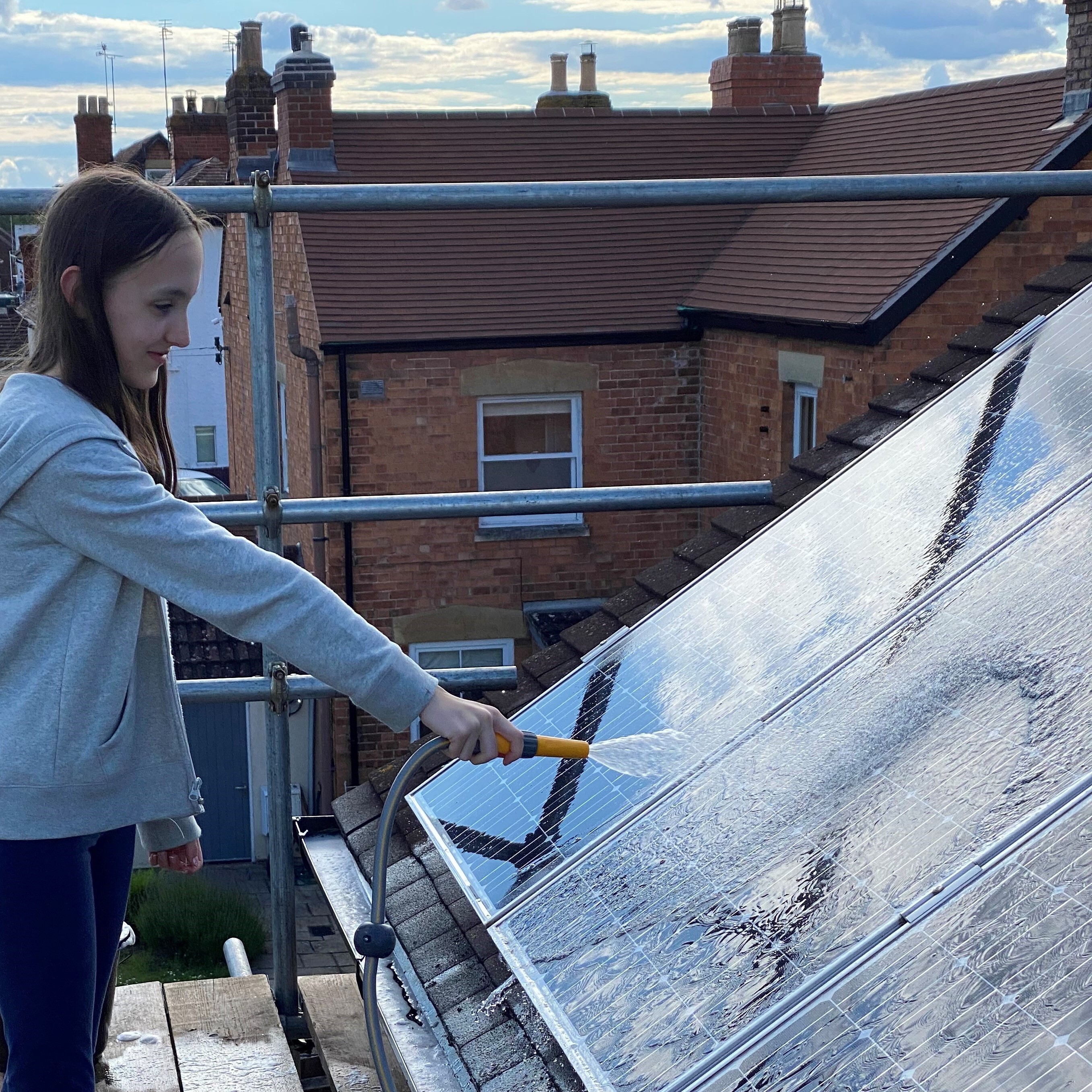 Young girl washes solar panels with a garden hose